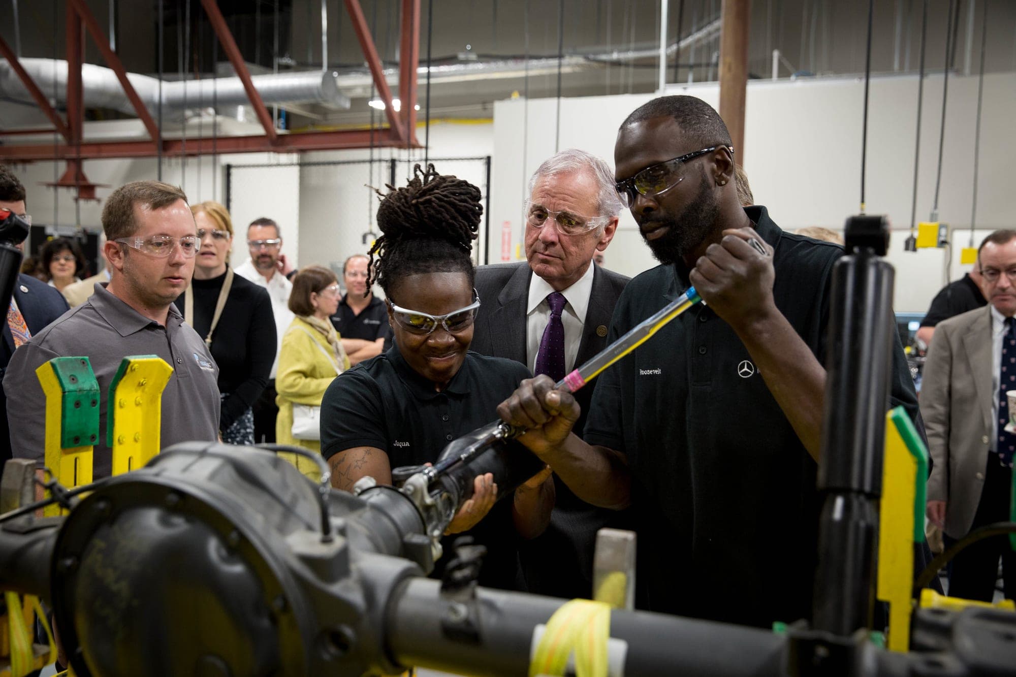 Two people in Mercedes-Benz shirts work on a vehicle axle at the readySC Mercedes-Benz Vans training facility at Trident Technical College as Gov. Henry McMaster looks on during a May 2017 tour.