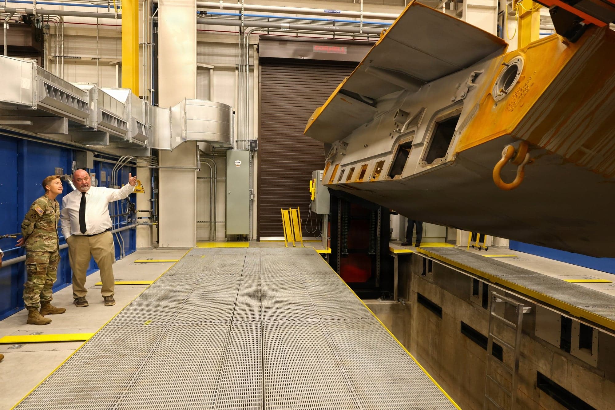 An M1 Abrams tank hull is turned into position in a new combat vehicle welding facility at Anniston Army Depot in Alabama on May 20, 2026, as Brig. Gen. Beth A. Behn, commanding general of the Army's Tank-automotive and Armaments Command, is briefed by weld supervisor Russell Holliday.